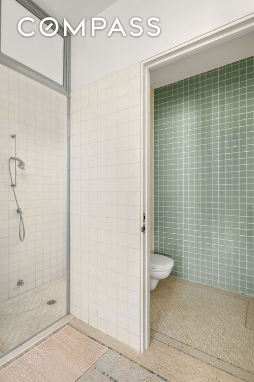 full bathroom with toilet, a stall shower, tile walls, and tile patterned floors