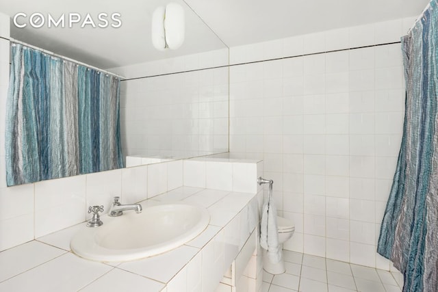 full bathroom featuring a shower with shower curtain, toilet, tile patterned floors, a sink, and tile walls