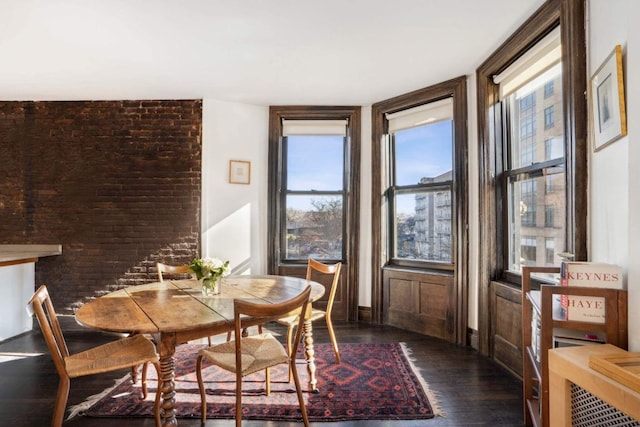 dining room with brick wall and dark wood-type flooring