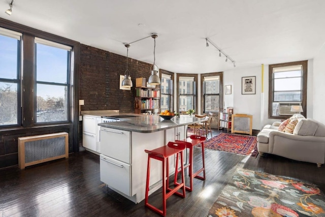 kitchen featuring white cabinets, radiator, decorative light fixtures, a peninsula, and a kitchen bar