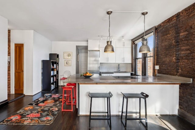 kitchen with built in fridge, pendant lighting, white cabinetry, a peninsula, and a kitchen bar