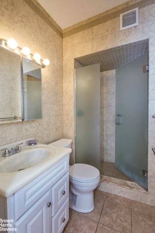 full bath with a stall shower, visible vents, toilet, vanity, and tile walls