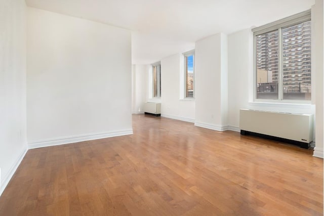 spare room with baseboards, radiator heating unit, and wood finished floors