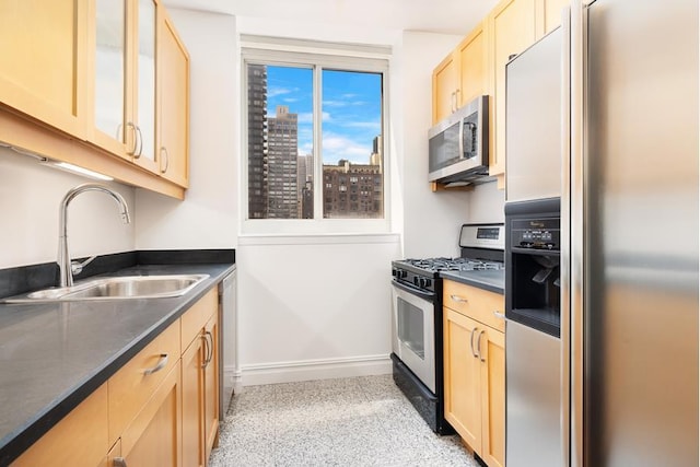 kitchen featuring dark countertops, glass insert cabinets, stainless steel appliances, light brown cabinets, and a sink