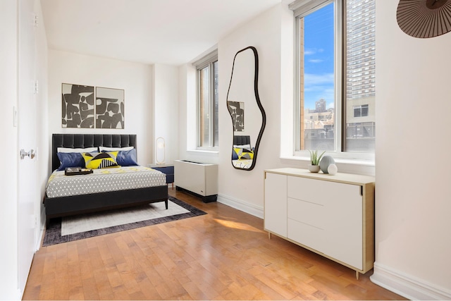 bedroom featuring radiator heating unit, light wood-style flooring, and baseboards