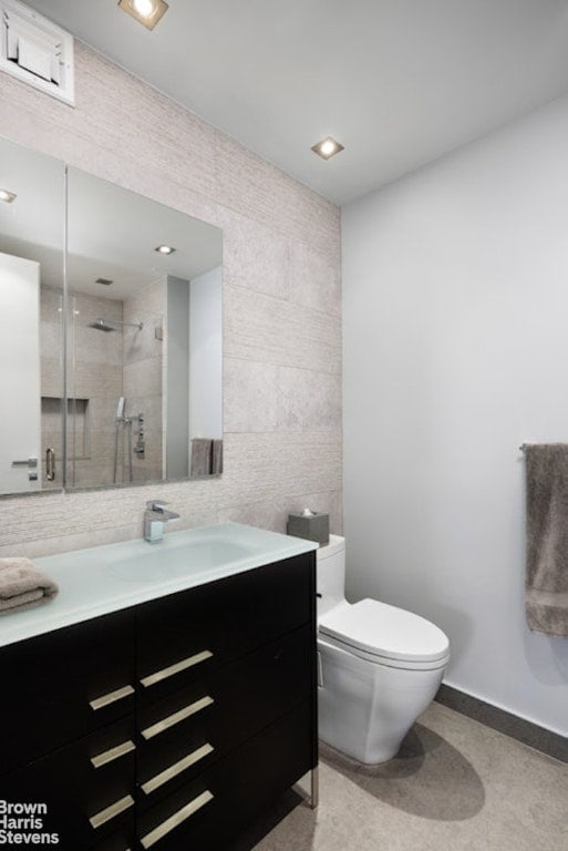 bathroom featuring toilet, tile walls, vanity, and tiled shower