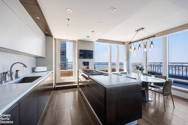 kitchen with pendant lighting, sink, dark wood-type flooring, white cabinetry, and a kitchen island