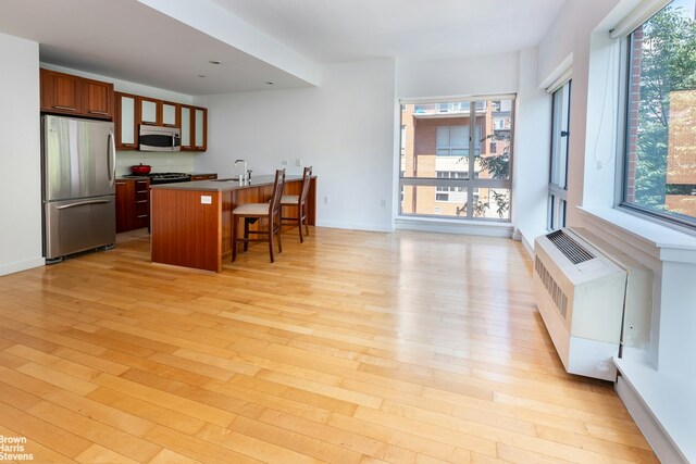 kitchen with dark countertops, radiator heating unit, appliances with stainless steel finishes, a kitchen breakfast bar, and light wood-style floors