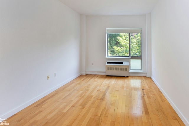 empty room with light wood-type flooring, baseboards, and radiator heating unit