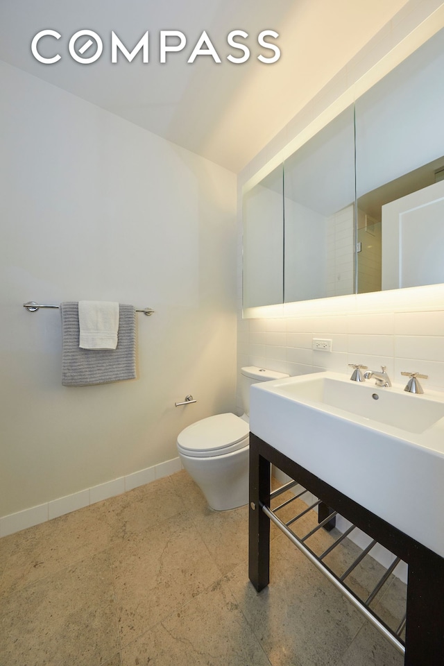 bathroom with decorative backsplash, toilet, vanity, and baseboards