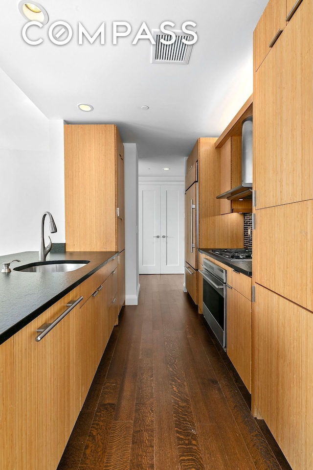 kitchen featuring dark wood finished floors, high end fridge, a sink, oven, and dark countertops