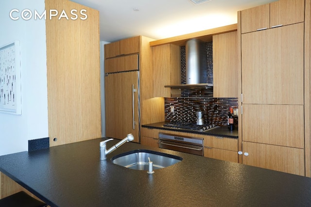 kitchen featuring sink, wall oven, paneled refrigerator, stainless steel gas cooktop, and wall chimney exhaust hood