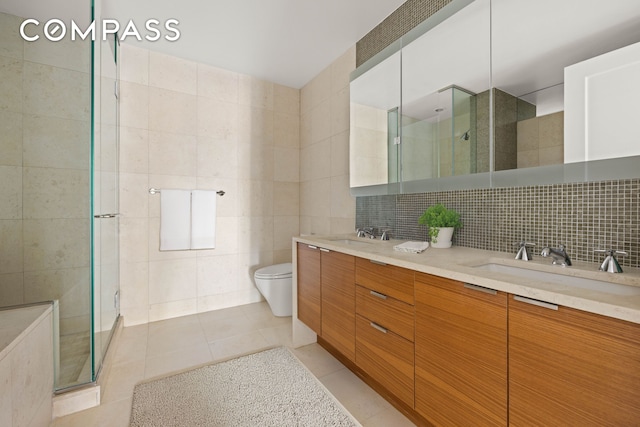 full bathroom with tile patterned floors, a stall shower, tile walls, and a sink