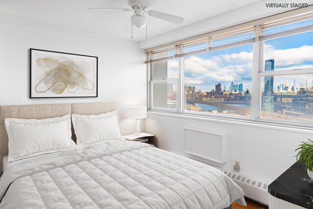 bedroom featuring ceiling fan, baseboard heating, and a city view