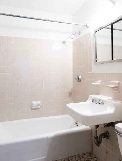 full bathroom featuring tiled shower / bath combo, sink, tile walls, and toilet