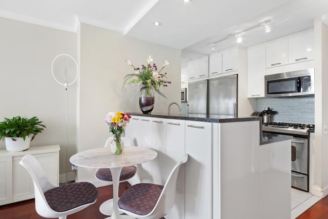 kitchen with hardwood / wood-style flooring, stainless steel appliances, white cabinets, decorative backsplash, and crown molding