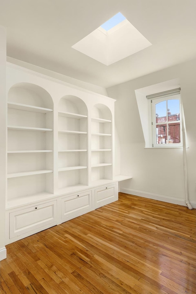 bonus room featuring built in shelves, baseboards, a skylight, and hardwood / wood-style flooring