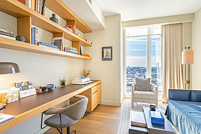 office area featuring baseboards, built in desk, light wood-style flooring, and a city view