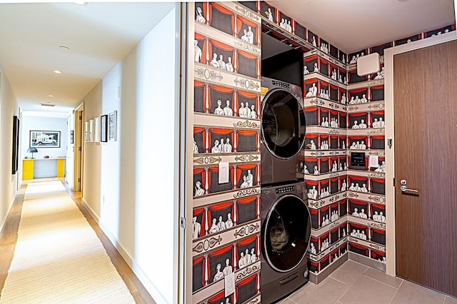 clothes washing area featuring laundry area, baseboards, stacked washer / dryer, and tile patterned floors