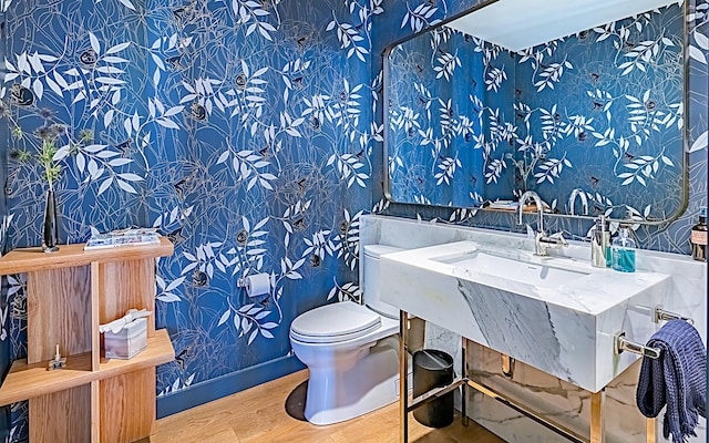 bathroom with baseboards, a sink, toilet, and wallpapered walls