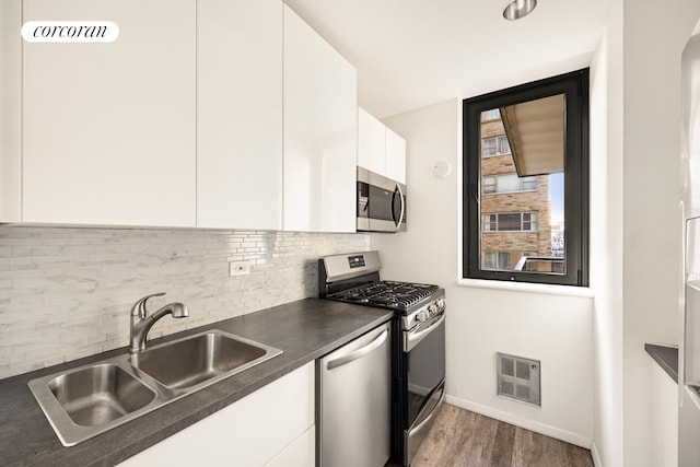 100 United Nations Plz Unit 7G, New York City, NY 10017 - kitchen with appliances with stainless steel finishes, a sink, dark countertops, white cabinetry, and dark wood-style flooring