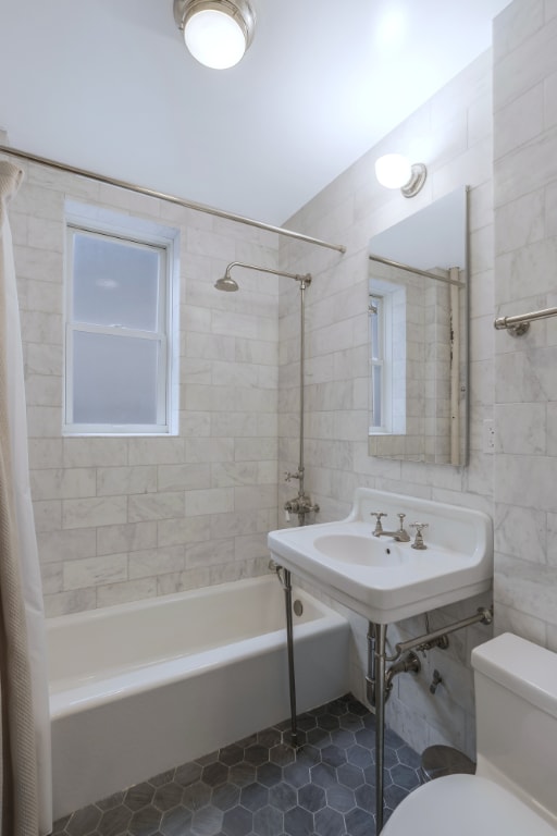 bathroom featuring tile walls, toilet, and shower / tub combo