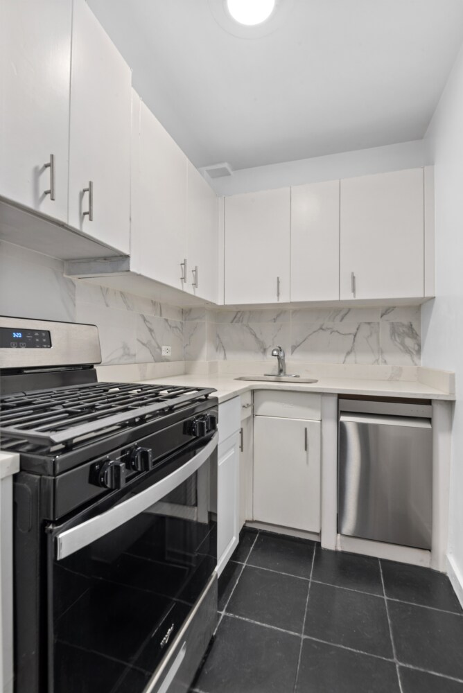 446 E 86th St Unit 2B, New York City, NY 10028 - kitchen with stainless steel appliances, white cabinetry, backsplash, and light countertops