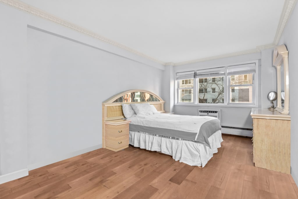 bedroom featuring hardwood / wood-style flooring, ornamental molding, a wall unit AC, and a baseboard heating unit