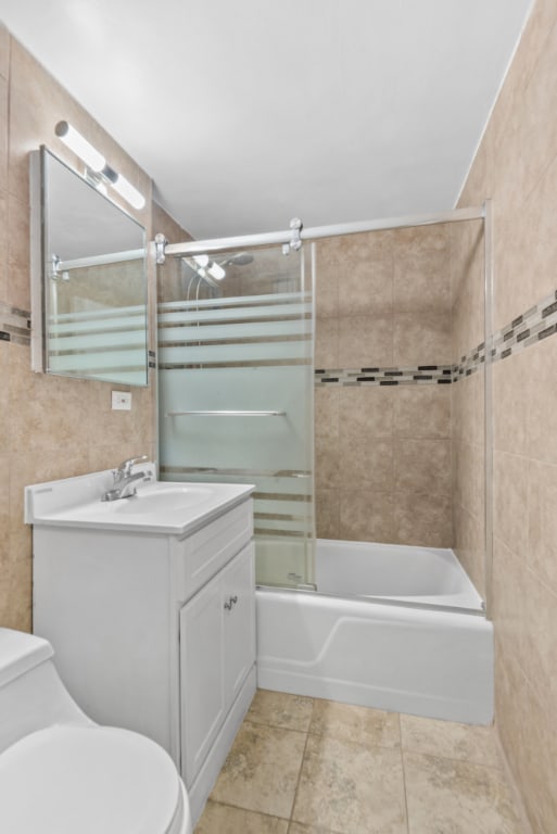 full bathroom with enclosed tub / shower combo, tile patterned flooring, tile walls, vanity, and toilet