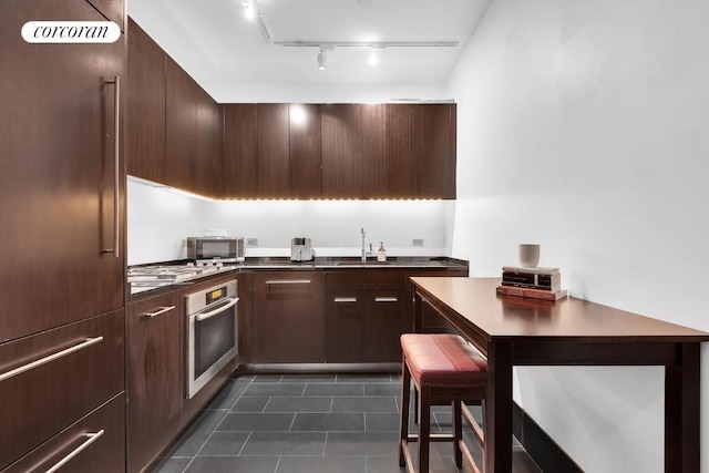 kitchen with sink, dark tile patterned floors, dark brown cabinetry, stainless steel appliances, and track lighting