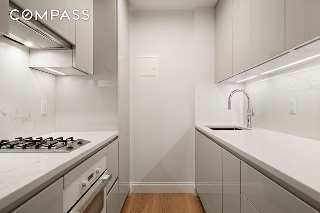 kitchen with appliances with stainless steel finishes, a sink, extractor fan, light wood-type flooring, and baseboards