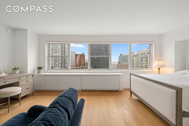 bedroom with a view of city, multiple windows, and light wood finished floors