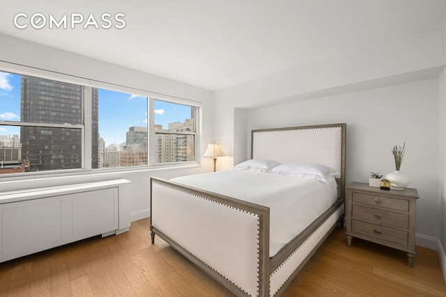 bedroom with light wood-style floors, a view of city, and baseboards