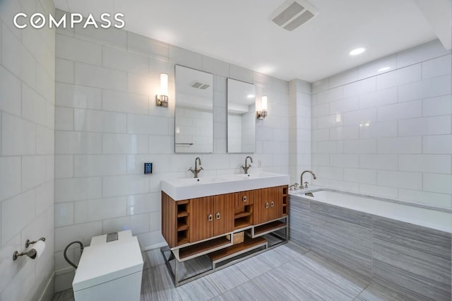 full bath with visible vents, a garden tub, a sink, tile walls, and double vanity