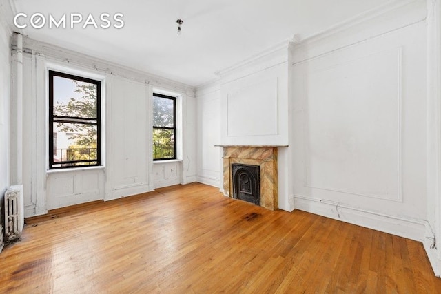 unfurnished living room featuring crown molding, radiator heating unit, a fireplace, and light wood-type flooring