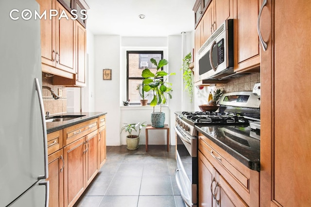 kitchen featuring appliances with stainless steel finishes, sink, backsplash, and dark stone counters