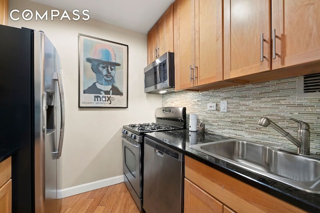 kitchen with stainless steel appliances, sink, decorative backsplash, and light hardwood / wood-style flooring