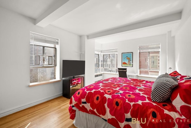 bedroom with radiator heating unit, beam ceiling, multiple windows, and light wood-type flooring