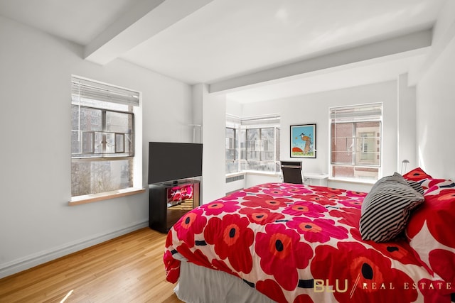 bedroom with radiator heating unit, beam ceiling, multiple windows, and light wood-style flooring