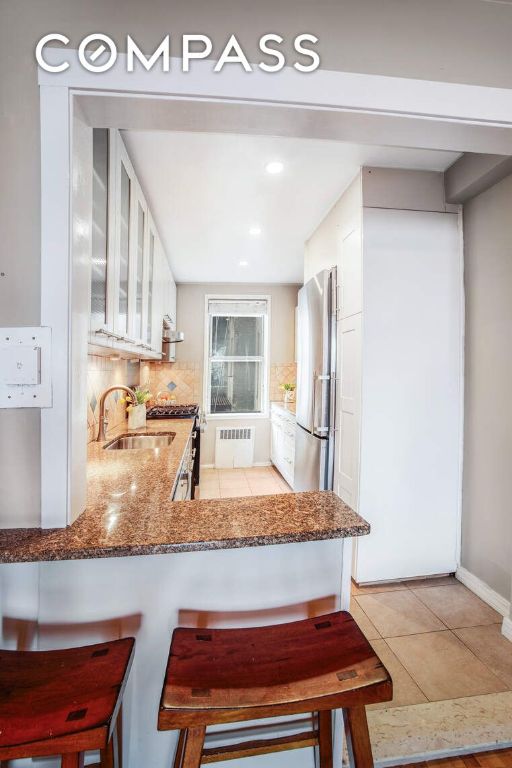 kitchen featuring stainless steel fridge, radiator, glass insert cabinets, a peninsula, and white cabinetry