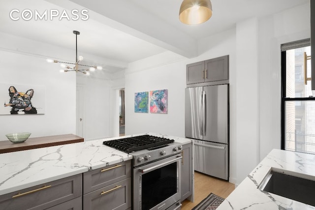 kitchen with light stone counters, a chandelier, light wood-type flooring, stainless steel appliances, and beam ceiling