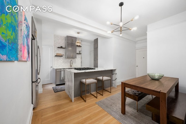 kitchen featuring hanging light fixtures, light wood-type flooring, kitchen peninsula, stainless steel appliances, and decorative backsplash