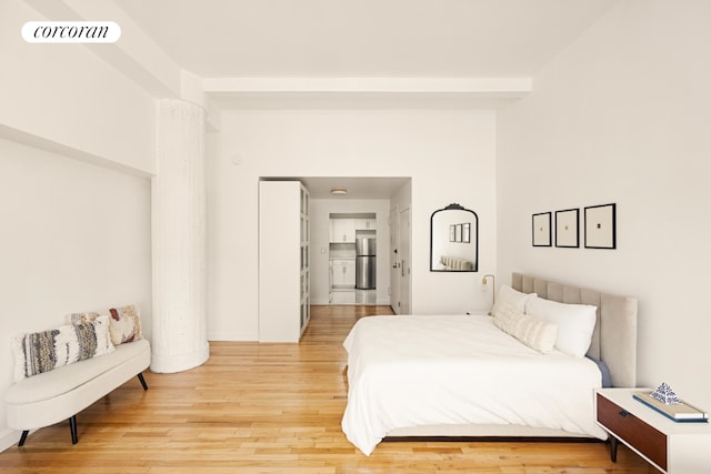 bedroom featuring wood-type flooring, stainless steel fridge, and beam ceiling