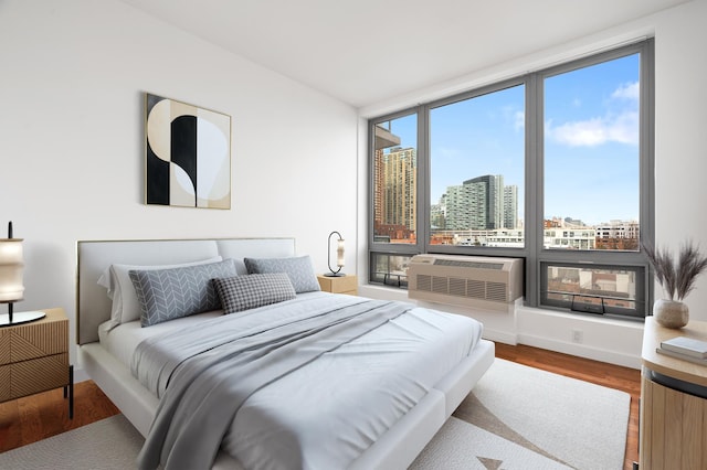 bedroom with a city view, an AC wall unit, and wood finished floors