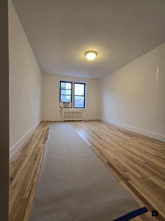 unfurnished room with radiator heating unit, baseboards, and wood finished floors