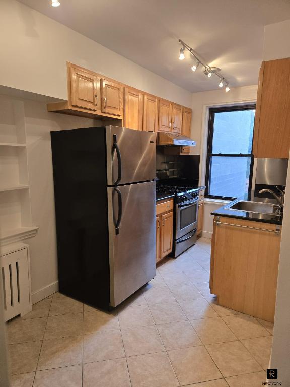 kitchen featuring dark countertops, appliances with stainless steel finishes, light brown cabinets, a sink, and under cabinet range hood