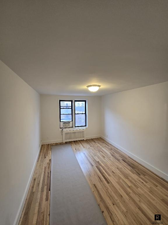 spare room with baseboards, radiator heating unit, and light wood-style floors