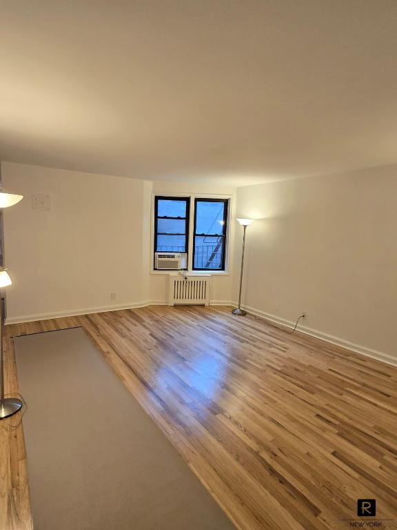 empty room with cooling unit, baseboards, radiator heating unit, and wood finished floors