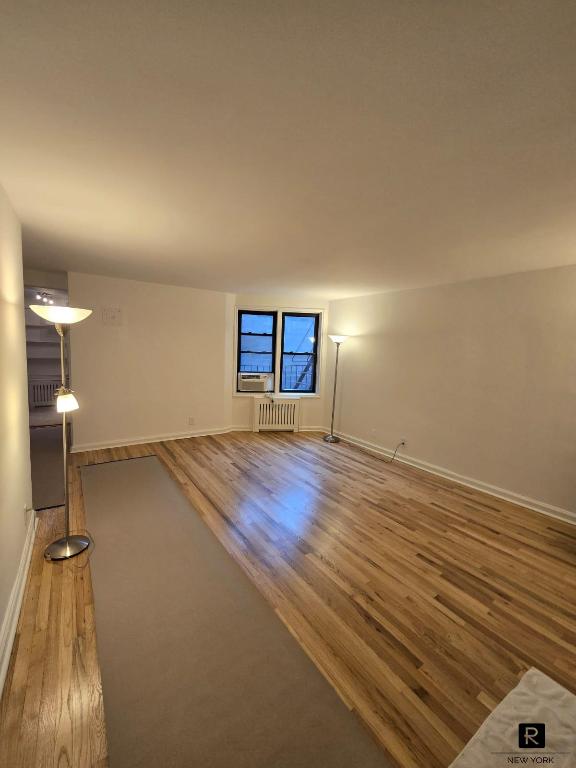 spare room featuring baseboards, radiator heating unit, and wood finished floors