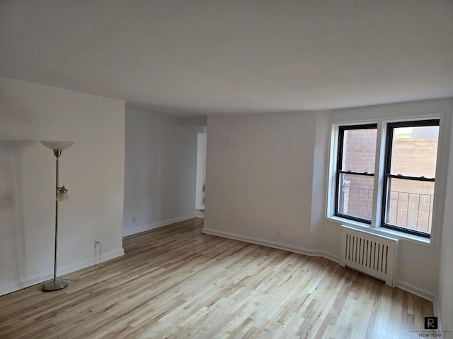 spare room featuring light wood-style floors, baseboards, and radiator heating unit